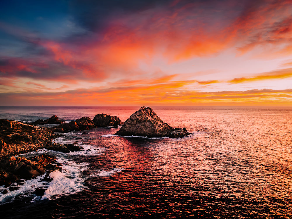 Aerial sunset photograph of Sugarloaf Rock, South West Western Australia, with deep orange and pink sky reflecting on the ocean.